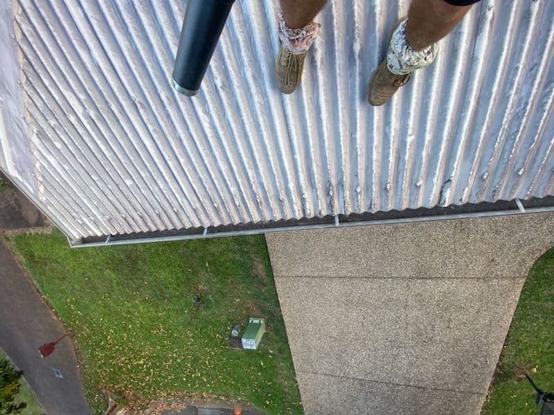 Cleared roof gutter feeding an open downpipe, seen from the roof edge
